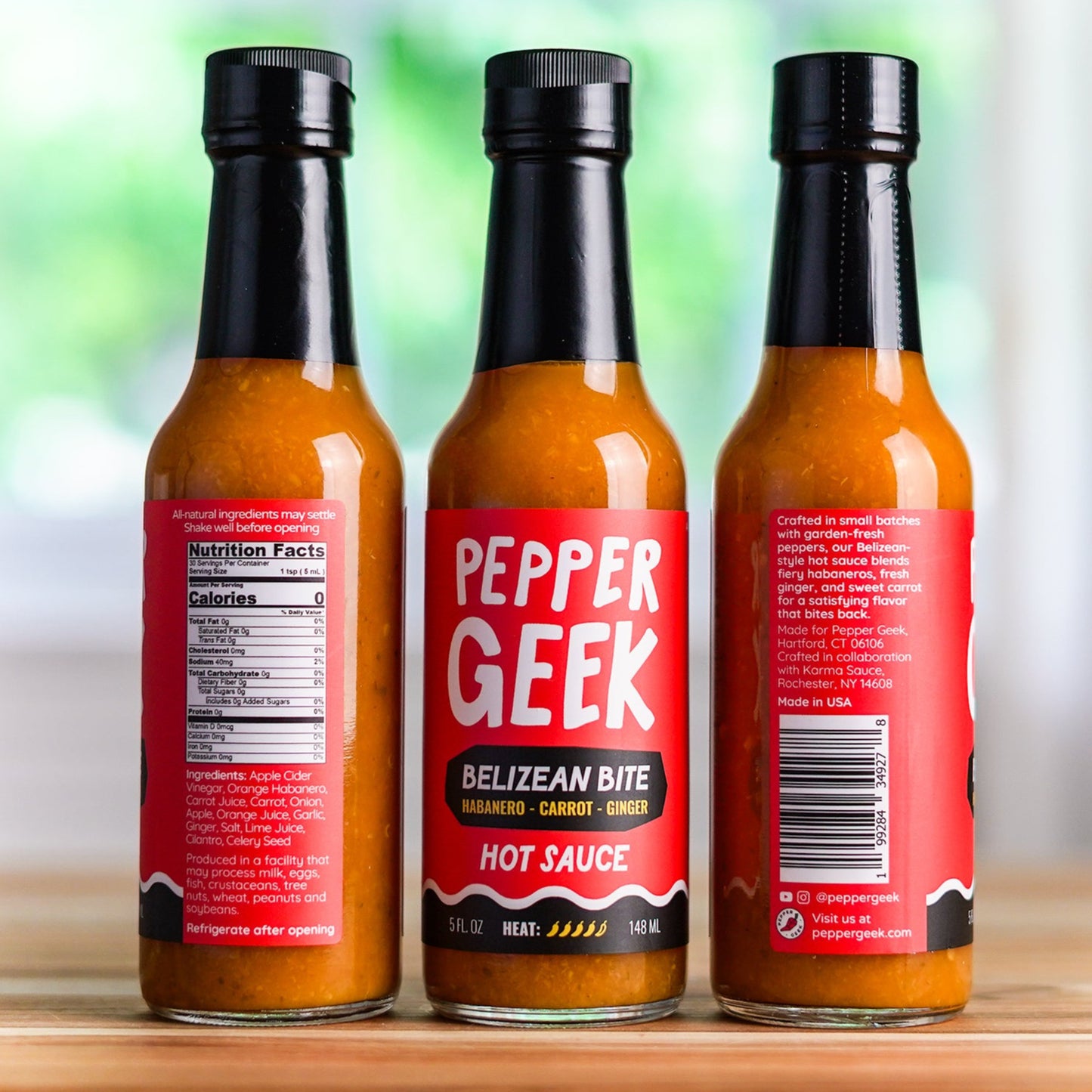 Three bottles of Pepper Geek hot sauce on a wooden surface with a blurred natural background